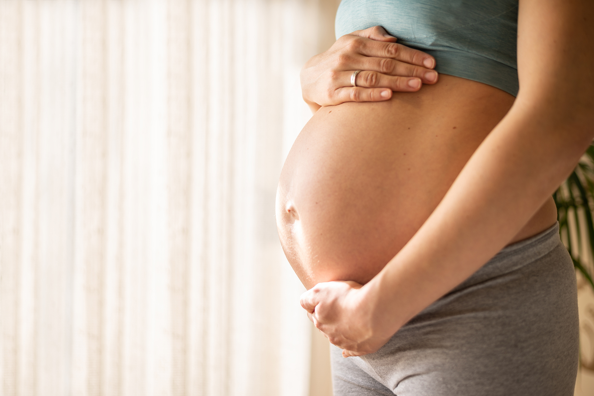 Womans bare pregnant belly being cradled by her arms