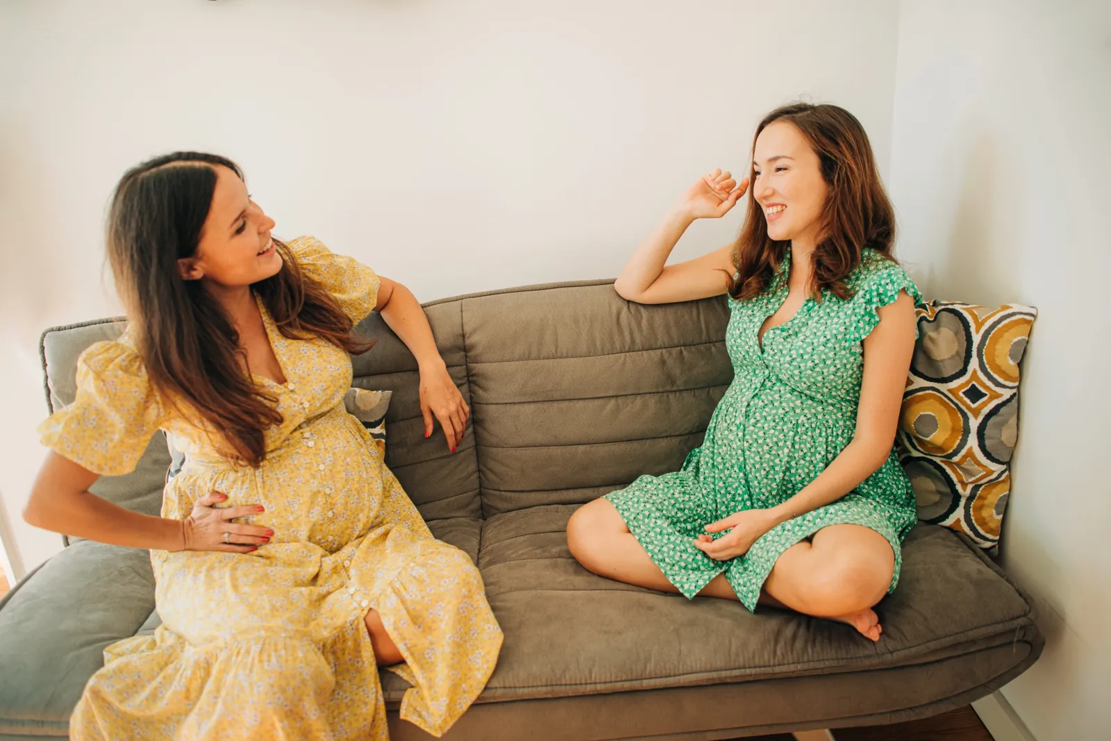 two pregnant women sitting on a couch talking to each other
