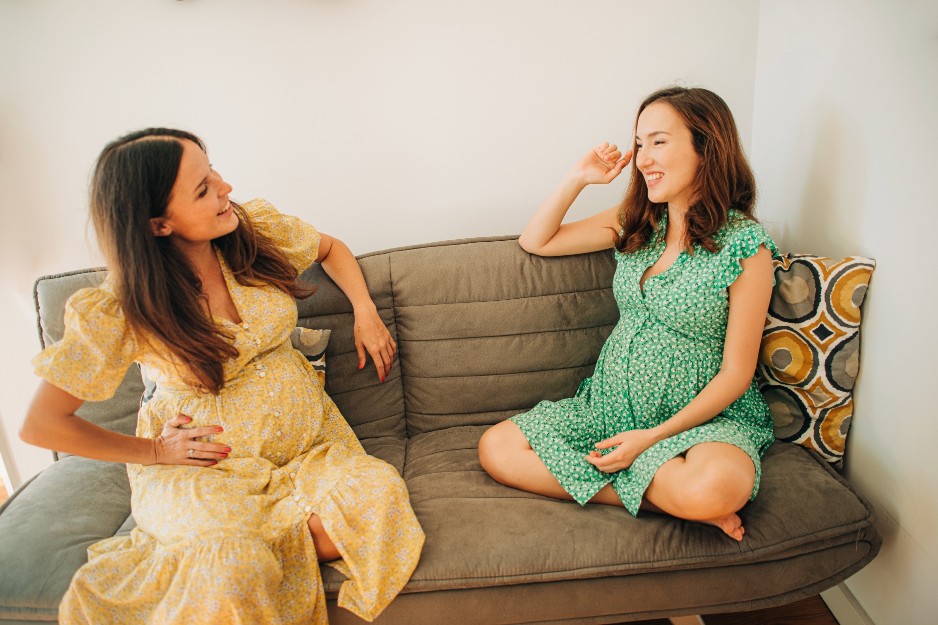 two pregnant women sitting on a couch talking to each other