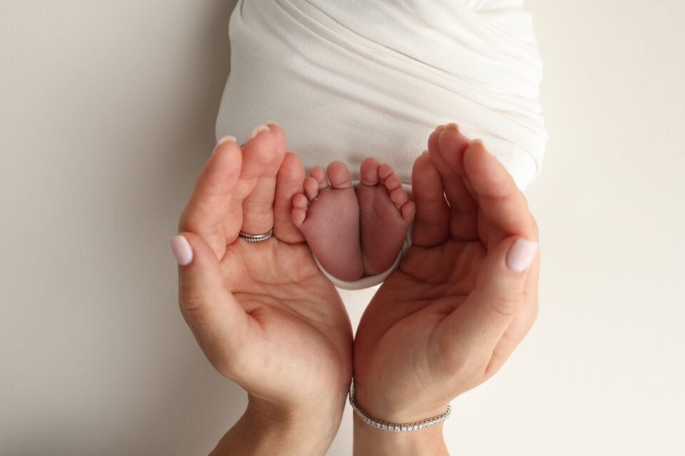 a father and mother hold the feet of a newborn child
