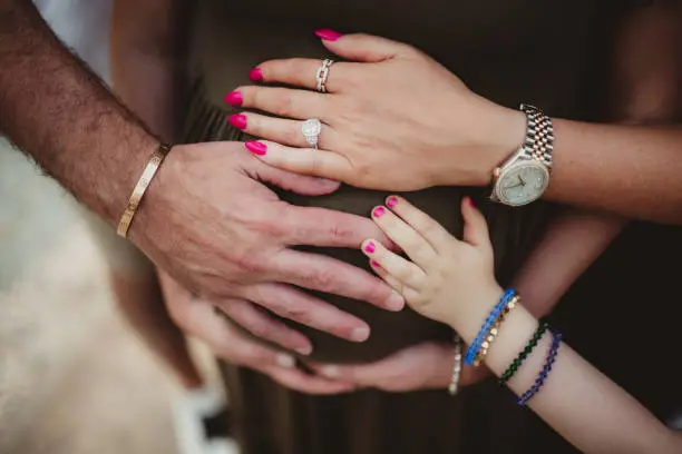 Hands with jewelry gently rest on a pregnant belly, symbolizing family unity and anticipation. The scene conveys warmth and expectation.